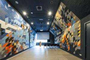 Vergaderruimte aan de Johan Huizingalaan met kleurrijke akoestische wandpanelen in geometrisch patroon en een projector met scherm.